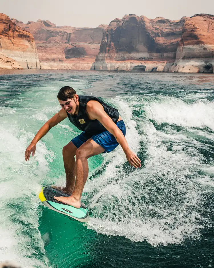 Photo: a rider mid-carve on the face of a boat wake, canyon wall above the water.